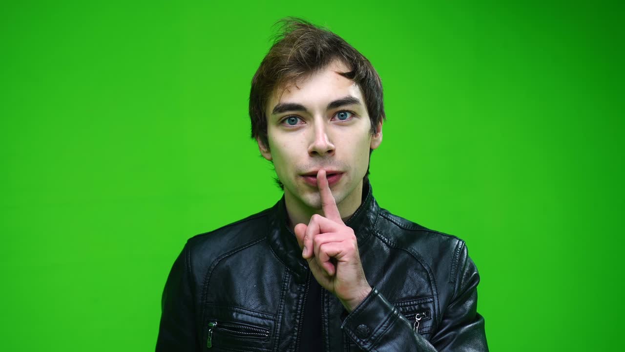 White man in leather jacket holding finger on his lips over green screen background.