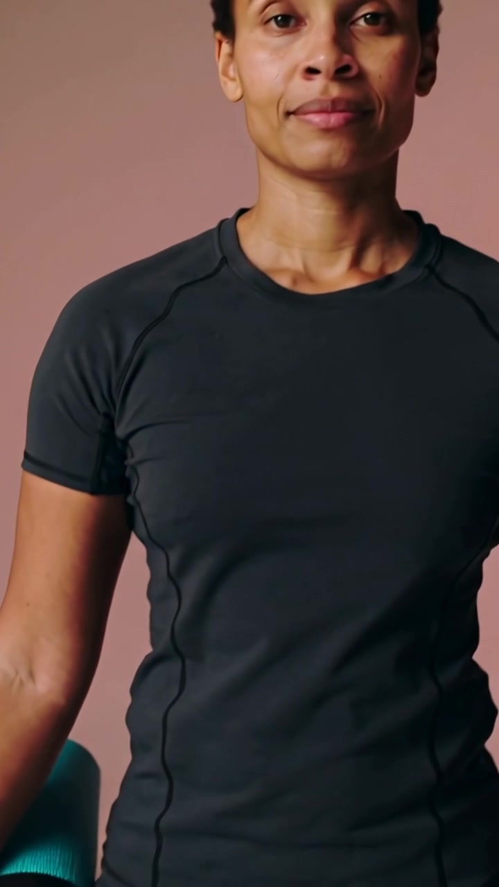 Video verticale: Panoramica che rivela una donna in forma in abbigliamento nero che sistema un tappetino color verde acqua, preparandosi per lo yoga.