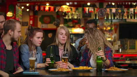 a large group of friends in the bar sitting at the table laughing and chatting drinking beer.