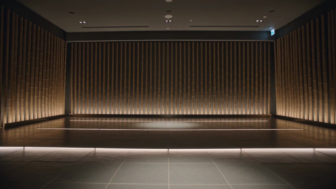 Recording camera framing empty raised wood stage in hall with slatted wall, LEDs glowing for demo