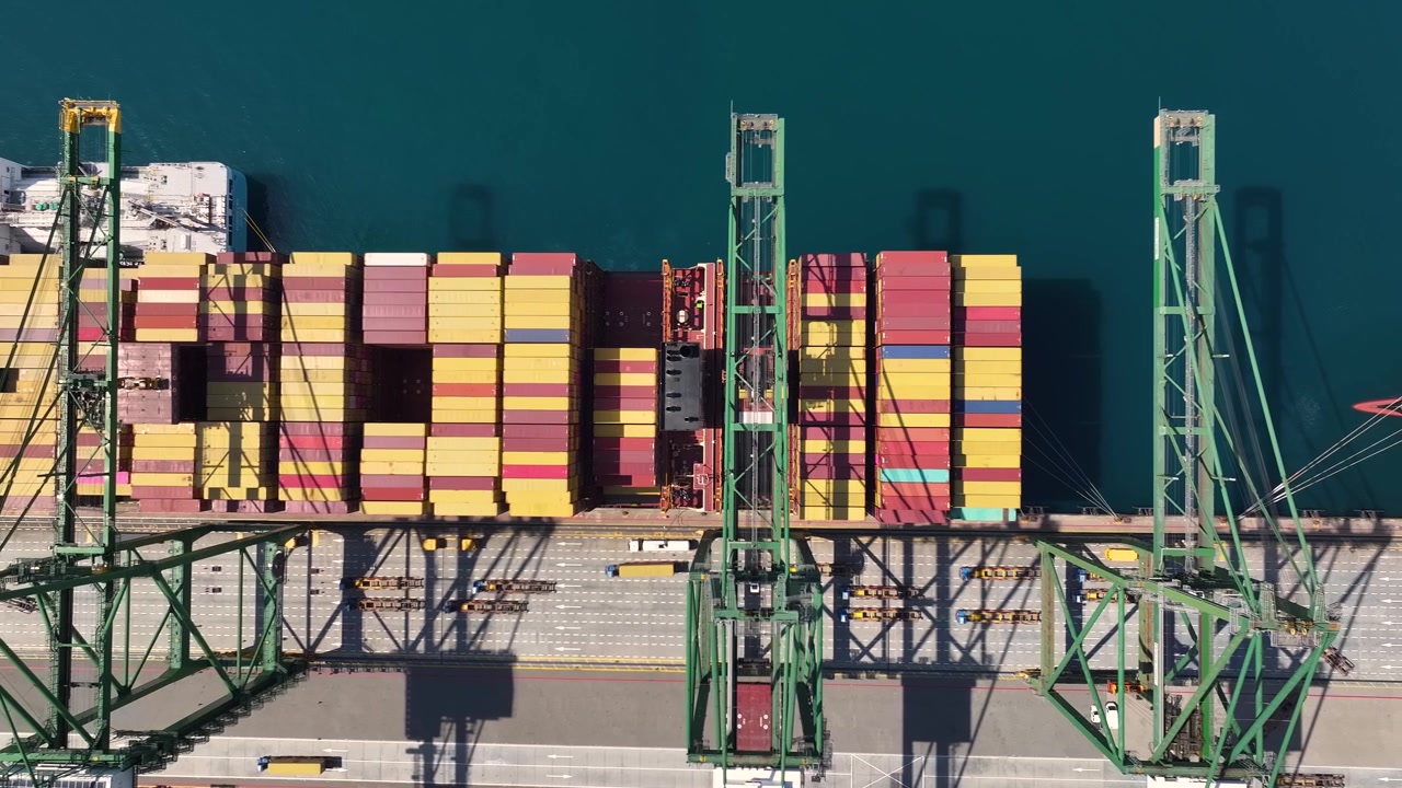 Lastcontainere er stablet på en shippingterminal. Kraner er placeret til laste- og losseoperationer. Shippingoverbelastning påvirker godstransporten. Forsinkelser påvirker den globale handel.