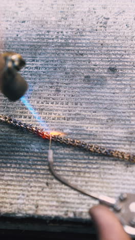 cu: young worker welds decorative gold chain with acetylene gas burner and special tool on white fireproof sheet closeup