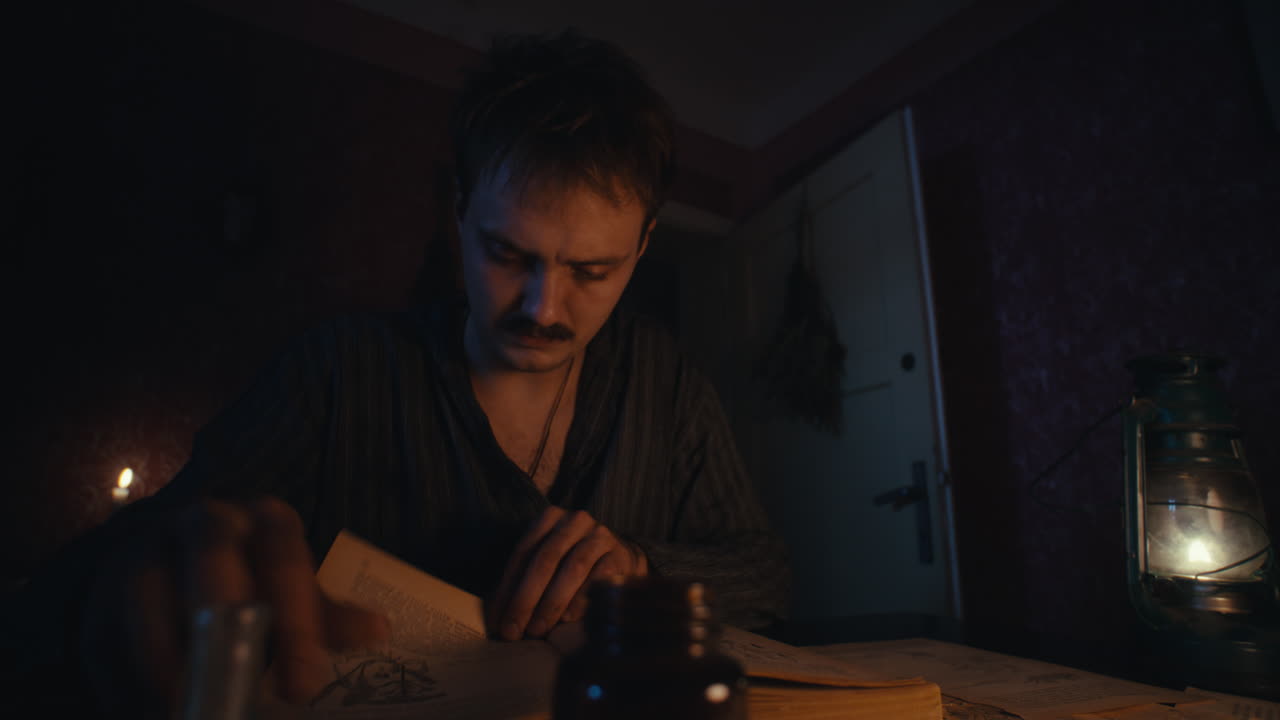 Man reading a book by candlelight and lantern in a dimly lit room