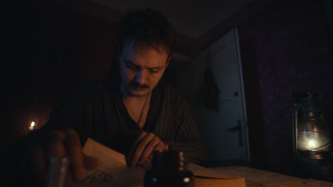 man reading a book by candlelight and lantern in a dimly lit room