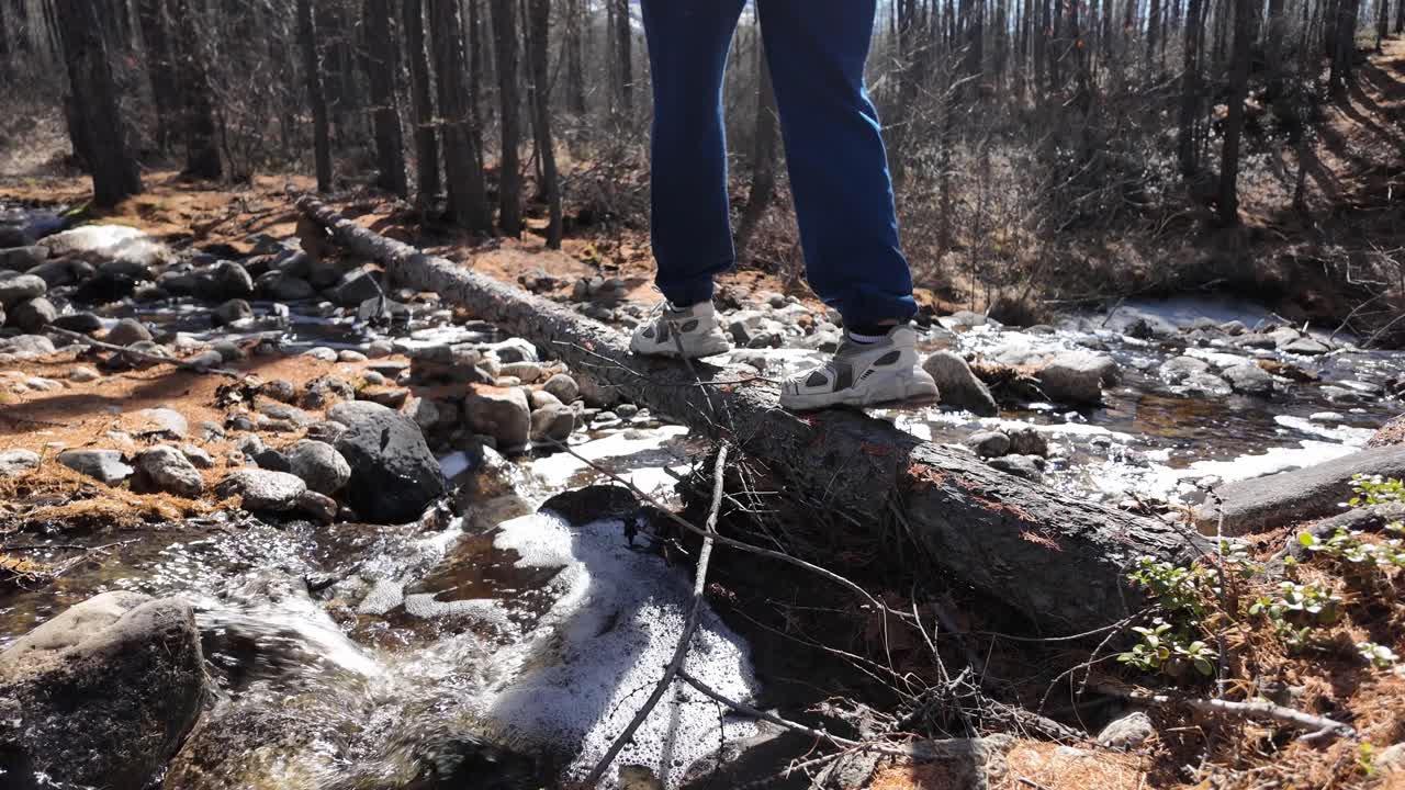한 사람이 숲 속에 쓰러진 나무를 가로질러 이동하여 자연 환경에서 균형과 민함을 보여줍니다.