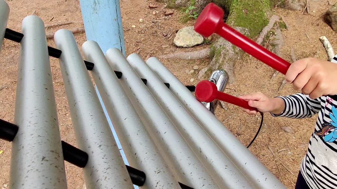 Young girl playing xylophone outdoors at playground - Learning music - Handheld static with focus on xylophone and hands - face barely visible