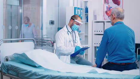 Doctor-in-mask-talking-with-senior-male-patient