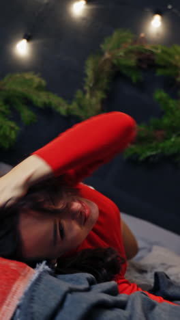 cheerful woman lying on bed in new year. young female with a pretty smile rolling over on bed happily on christmas decorated room background. vertical video