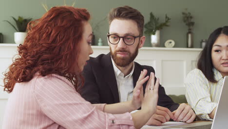 mujer joven explicando algo a sus dos colegas multiétnicos mientras se sienta a la mesa