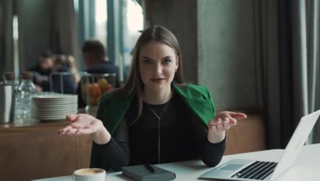 serious,-beautiful-young-woman-sitting-in-a-stylish-restaurant-dressed-in-business-attire-talks-and-argues-while-looking-into-the-camera