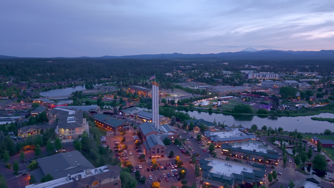 Bend Oregon Sunset. Drone flying by the Old Mill with smoke stacks, restaurants and businesses during evening blue hour.