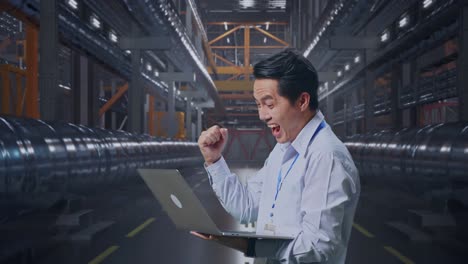 side view of an asian male professional worker standing with his laptop with metal pipes, he raises his fist up with screaming goal after typed on the laptop
