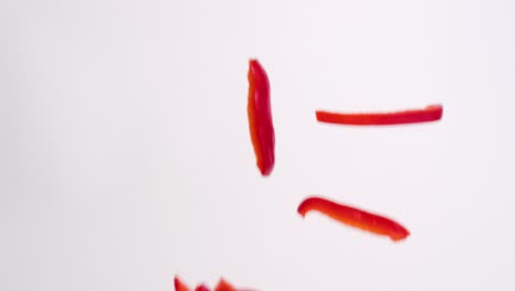 julienne cut sliced red bell pepper vegetable pieces raining down on white backdrop in slow motion