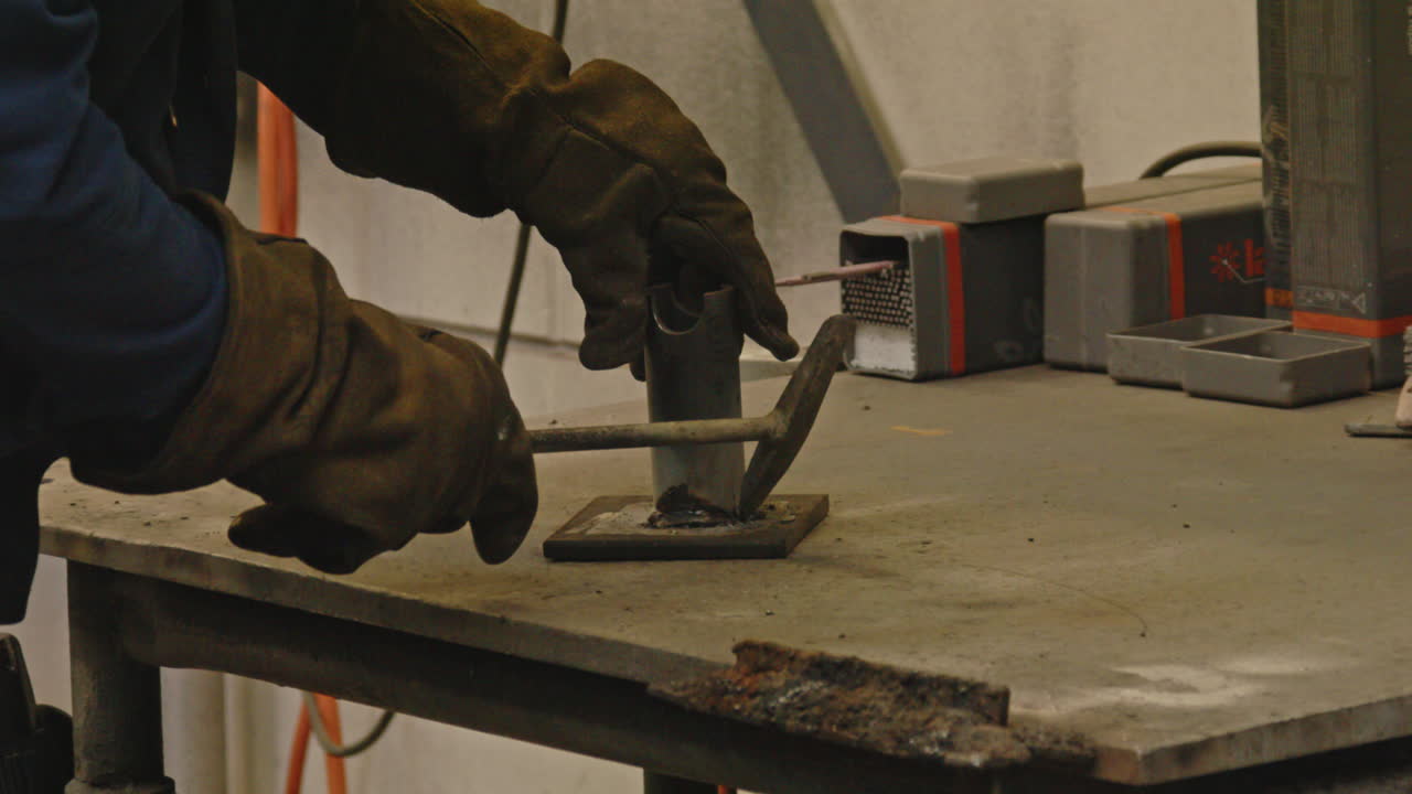 Metalworker using a hammer to knock of residue metal from welding seams on a piece of metal in slow motion