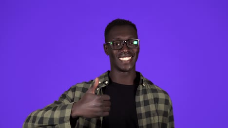 Happy,-smiling-african-american-man-in-good-mood-on-blue-background.-Man-in-stylish-glesses-gesturing-with-thumbs-up,-like-gesture-and-tooty-smiling---human-emotions