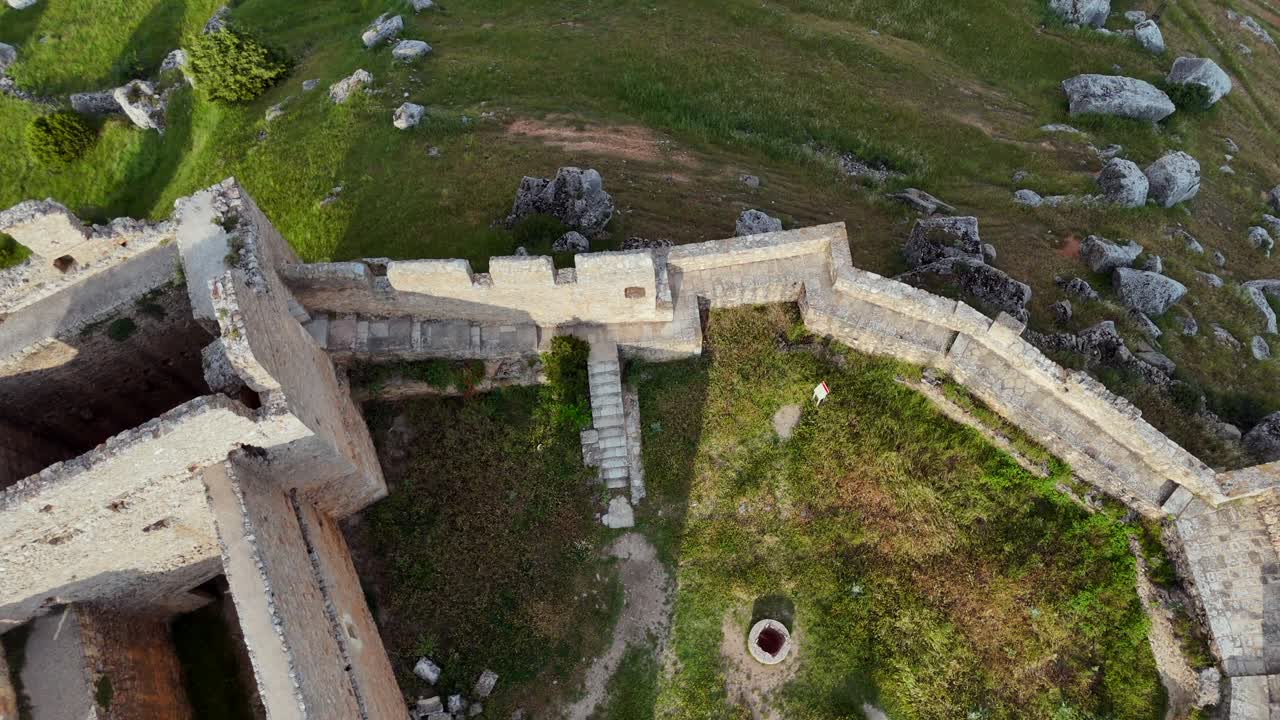An aerial drone view, tilting down, of the ruins of the massive and imposing fortress of Gormaz, in Soria province, built on a hill, surroended by green fileds.