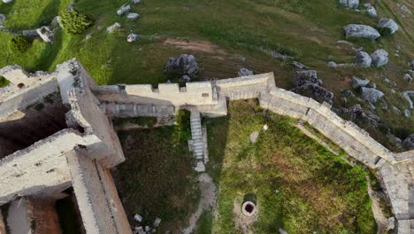 an aerial drone view, tilting down, of the ruins of the massive and imposing fortress of gormaz, in soria province, built on a hill, surroended by green fileds.