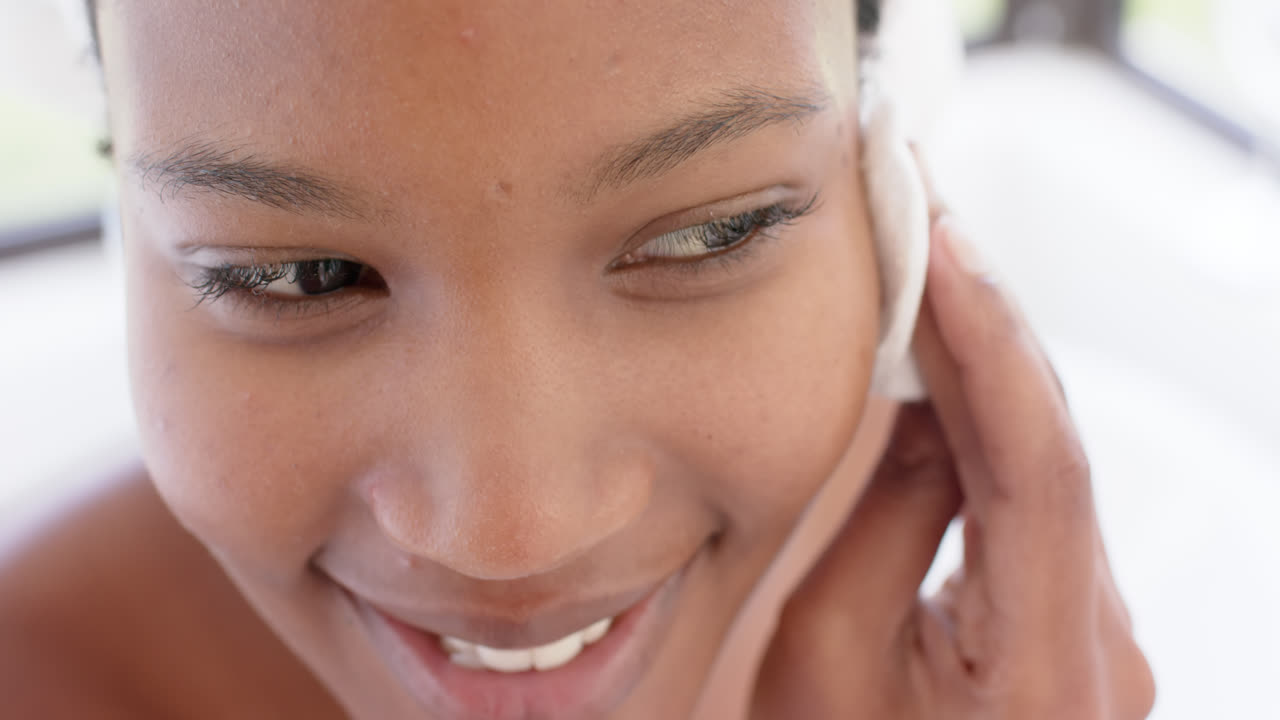 Happy biracial woman with towel on head washing her face, slow motion