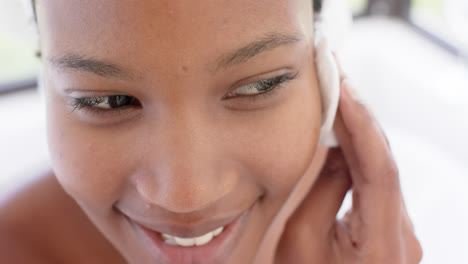 happy biracial woman with towel on head washing her face, slow motion