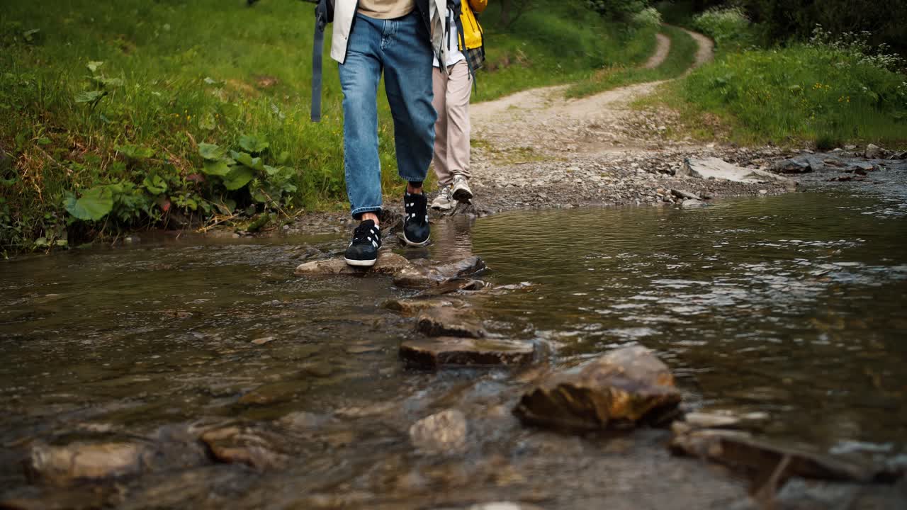 disparo en primer plano de un chico y una chica cruzando un río de montaña a lo largo de un camino especial hecho de piedras durante su caminata a través de los bosques de montaña