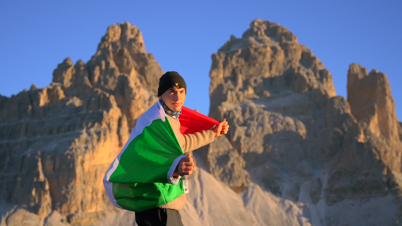 imágenes filmadas en rifugio auronzo, tri cine en las montañas de los dolomitas italianos con un hombre moviéndose y sosteniendo una bandera italiana y con hermosas montañas en el fondo, filmadas al amanecer en 4k