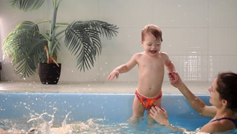 Dos-Bebés-Se-Ríen-En-La-Piscina-Y-Saltan-Al-Agua-Aplaudiendo