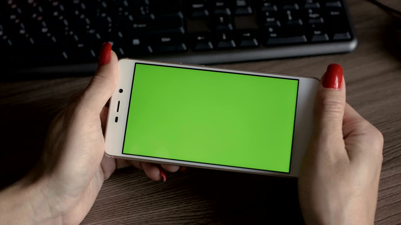 mujer mirando un teléfono inteligente con pantalla verde sentada en el escritorio de la oficina. mujer de negocios usando un teléfono inteligente. 4k uhd. de cerca.