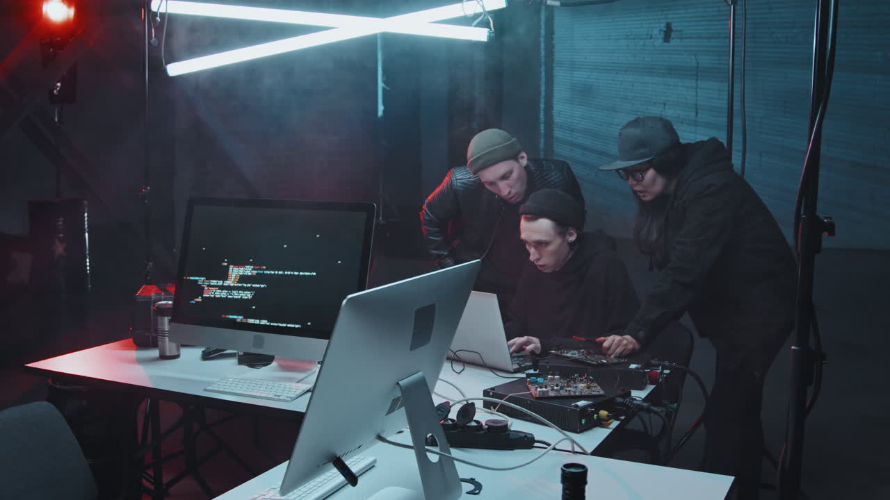 Three Hackers Talking and using Laptop in Dark Hideout