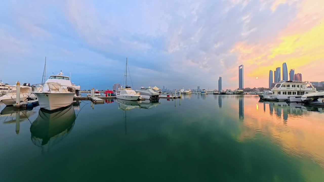 Sejlads ud fra Emirates Palace Marina under en gylden solopgang med reflekterende, roligt vand og byens skyline i baggrunden.