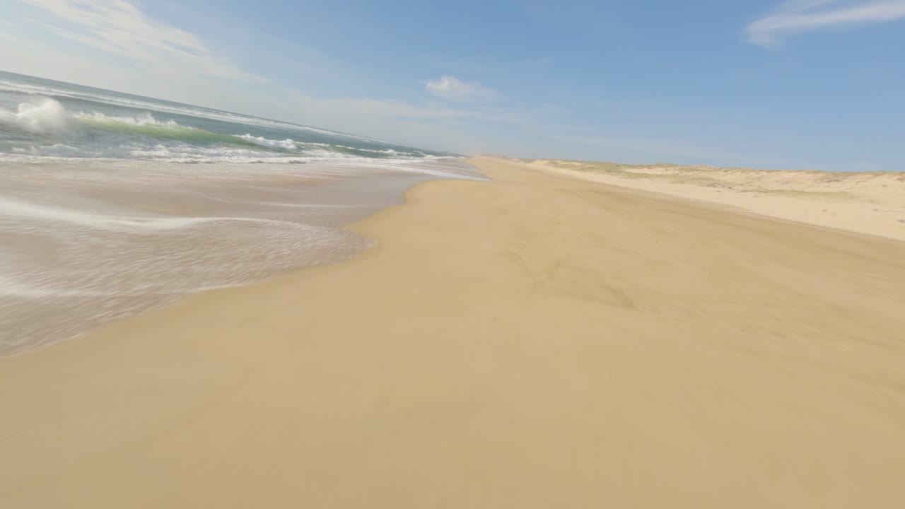 dron de carreras fpv aéreo volando bajo sobre la playa de arena y olas de espuma a lo largo de la costa, soustons en francia