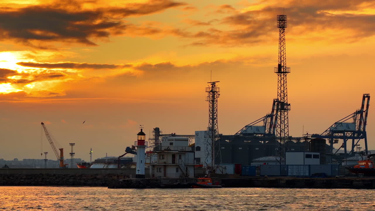 Vista al tramonto di un porto con gru e torri di comunicazione. La scena mostra un porto al tramonto con gru, torri di comunicazione e la silhouette di un faro.