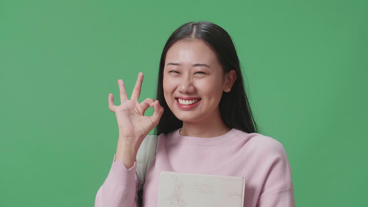 아시아 여성 학생이 책을 들고 녹색 스크린 스튜디오에서  제스처를 보여주고 있습니다.