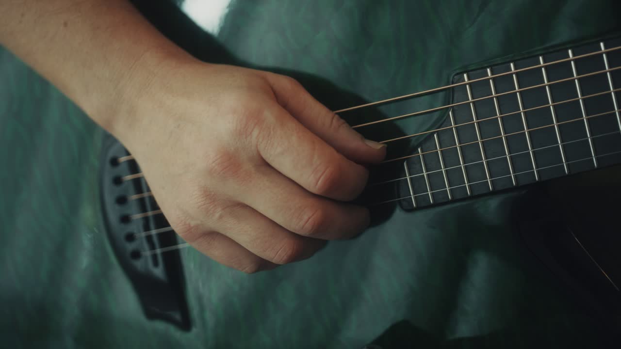 Primo piano di una mano che strimpella le corde di una chitarra acustica.