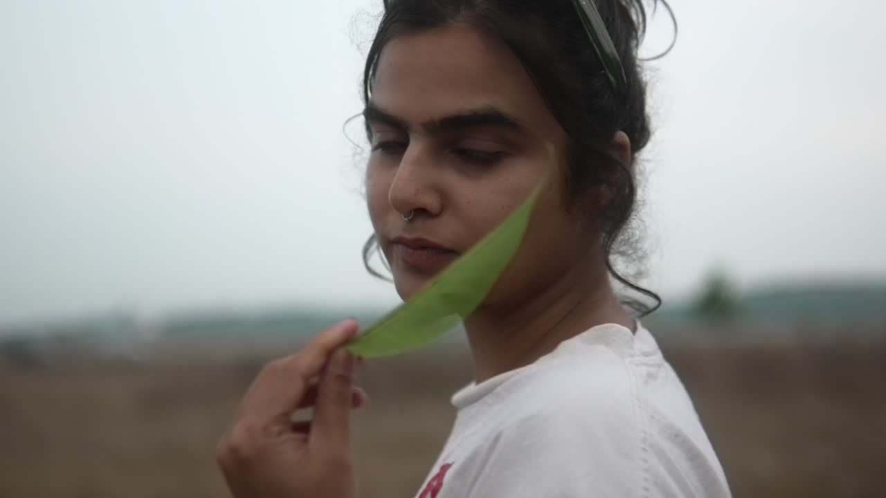 Young woman in a field holding a leaf, looking back over her shoulder
