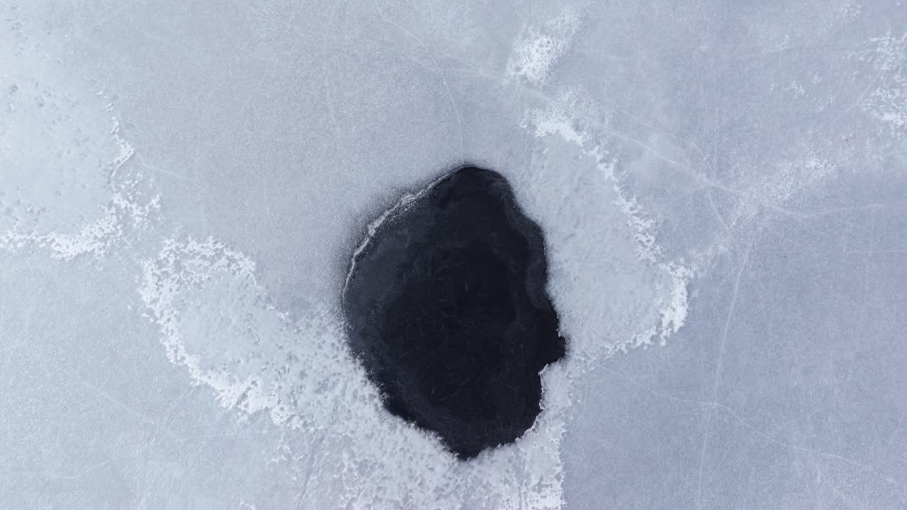 Melting lake ice forming dark patches on the surface. Sunny Spring weather. Aerial view revealing vastness of the lake.
