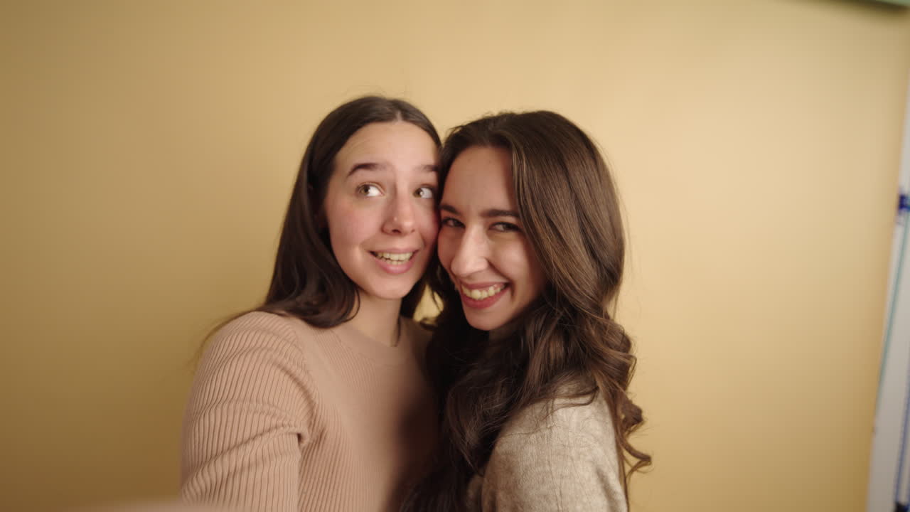 Two young women embracing looking at camera, while take a selfie smiling