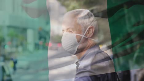 Animation-of-flag-of-nigeria-waving-over-caucasian-man-wearing-face-mask-in-city-street