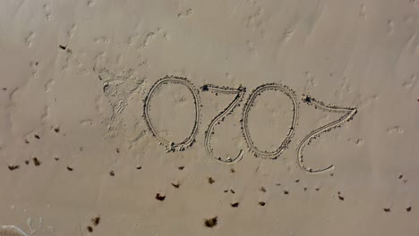 aerial camera showing a crazy twenty twenty inscribed in sand as it turns clockwise around and around