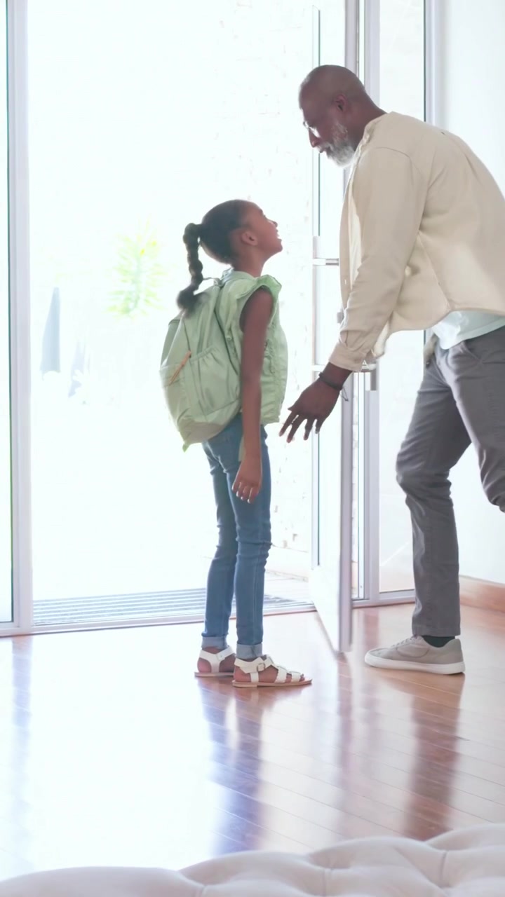 Dad kneeling, opening glass door, guiding girl home, girl taking mint-green backpack to counter