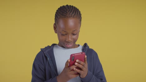 studio portrait of excited boy on asd spectrum gaming on mobile phone on yellow background 2