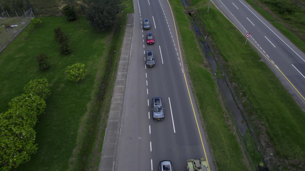 Overhead drone clip over lorry overtaking a queue of cars, moving along a two lane road lines with grass and bushes