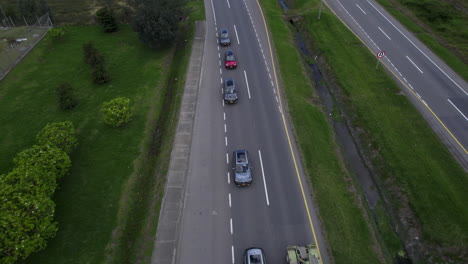 overhead drone clip over lorry overtaking a queue of cars, moving along a two lane road lines with grass and bushes