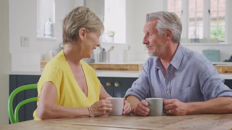 Küssendes-Rentnerehepaar,-Das-Zu-Hause-Am-Tisch-Sitzt-Und-Gemeinsam-Morgenkaffee-Trinkt