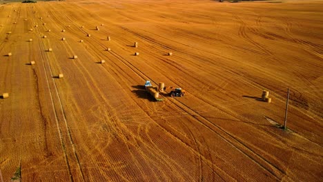 an aerial view of a large industrial brown field with a tractor collecting hay bales, zooming in