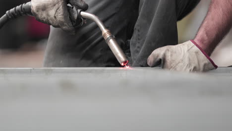 a skilled male worker wearing gloves holding a welding gun welding the metal edge then measures using pull-push rule for adequate length - welding factory - close-up shot, slow motion