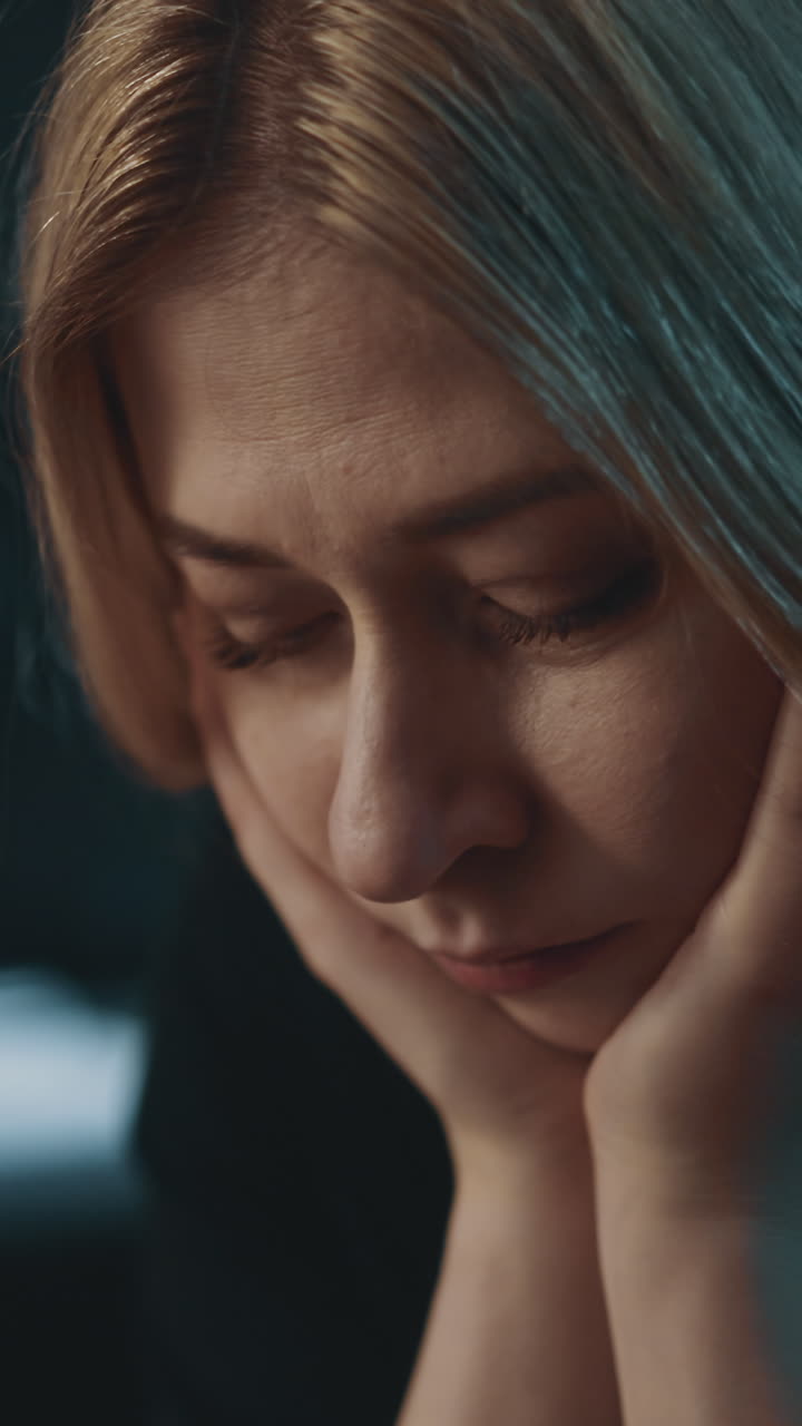 donna bionda sconvolta appoggiata ai palmi che soffre di sintomi di dura depressione su uno sfondo sfocato in una stanza buia a casa visione estrema ravvicinata rallentamento