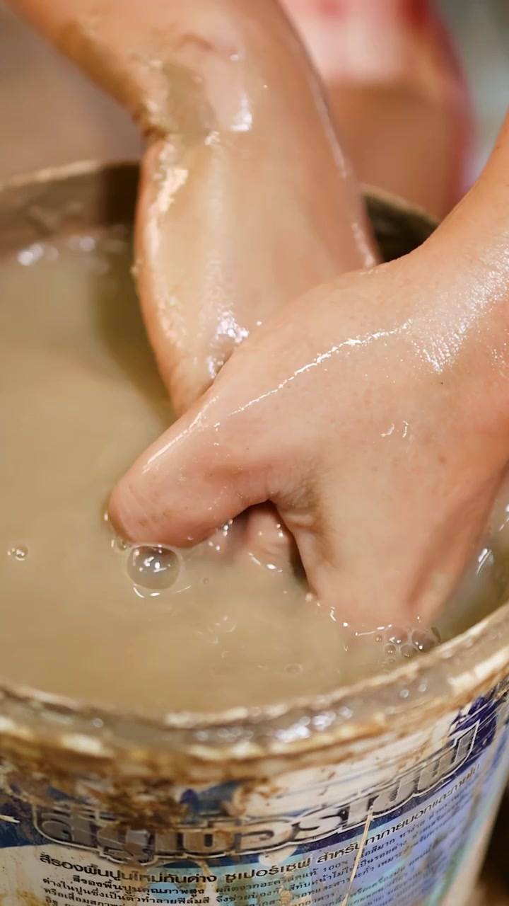 Primo piano delle mani che impastano fango e argilla bagnati dentro un secchio durante un laboratorio di ceramica.