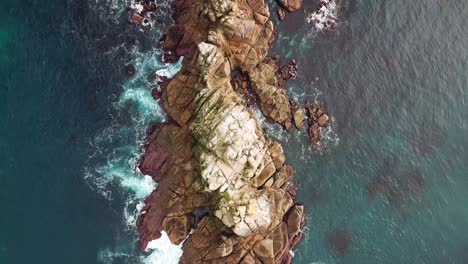 An-aerial-view-shot-of-Lands-End,-UK,-slowly-panning-over-the-land-as-waves-crash-peacefully-on-the-rocks-and-birds-fly-overhead