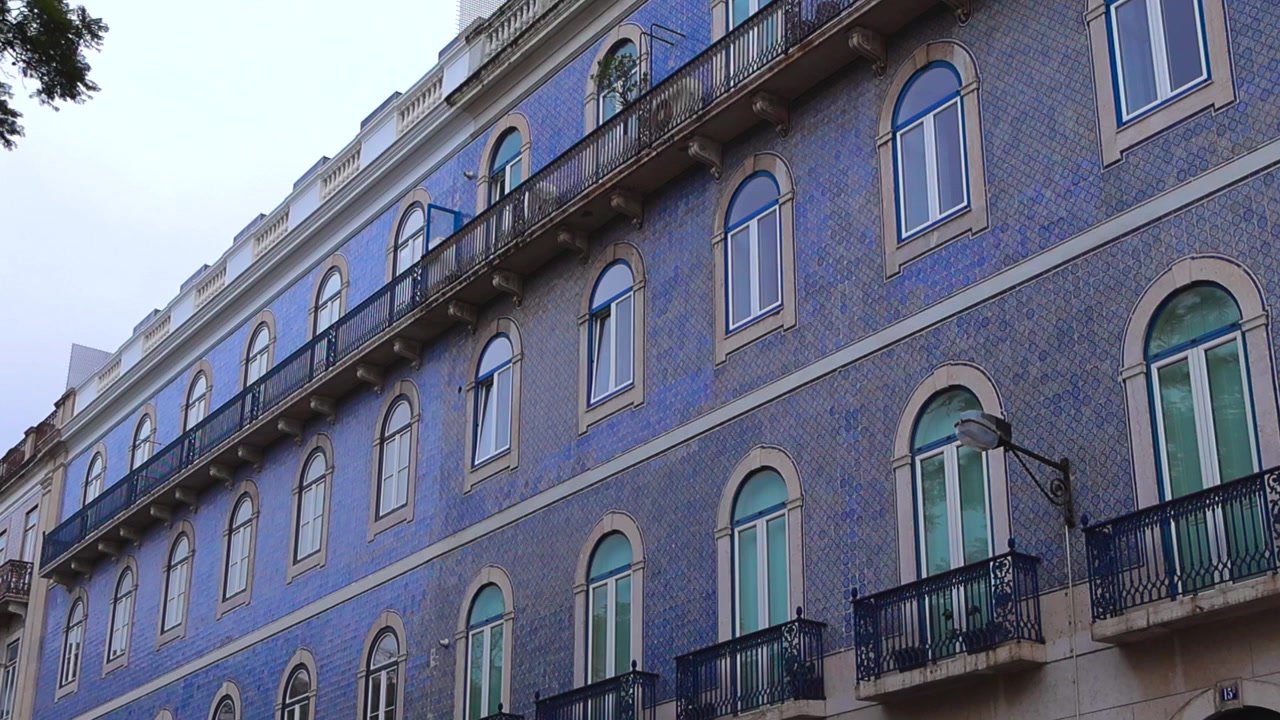 Sbalorditivo dettaglio architettonico della facciata di un tipico edificio piastrellato con azulejos blu a Lisbona, Portogallo, caratterizzata da balconi decorati e finestre ad arco sotto un cielo nuvoloso.