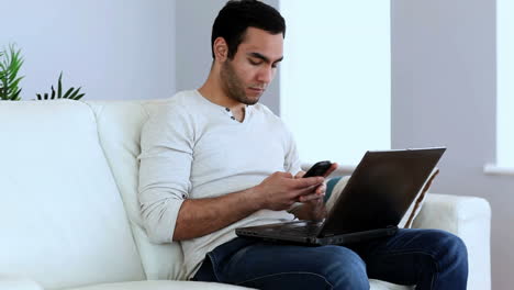 Man-using-his-smartphone-and-his-laptop